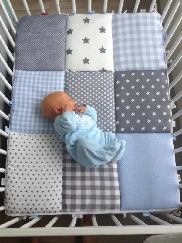 Een pasgeboren baby in een blauwe slaapzak ligt op een betegelde wiegrand.