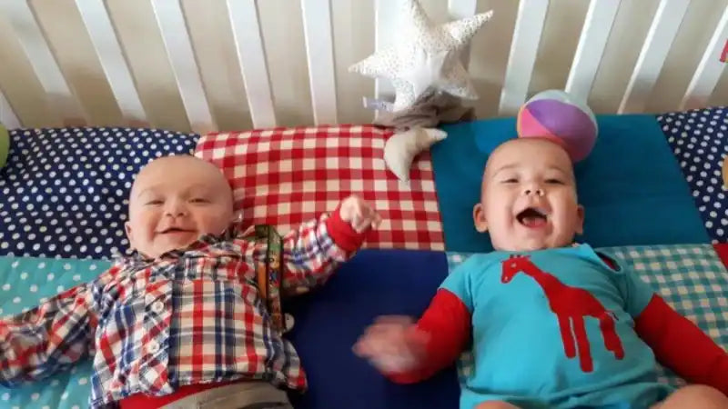 Twee lachende baby's liggen in een wieg.