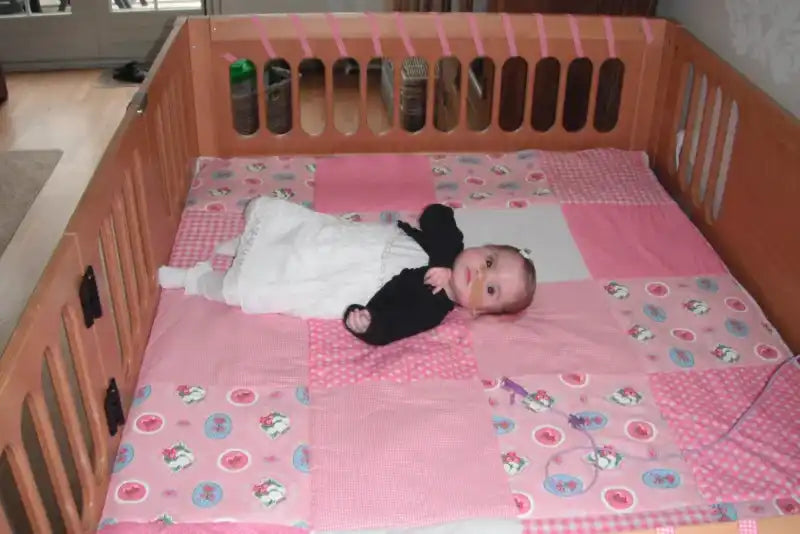 Baby in een houten wieg met roze beddengoed.
