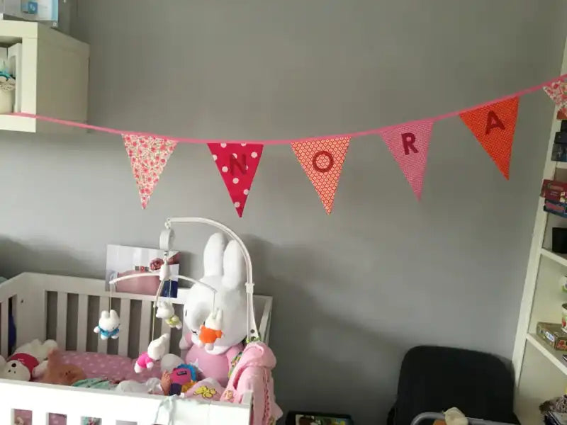 Een decoratieve stoffen banner met de naam ’NORA’ gespeld op afzonderlijke pennantlijnen.