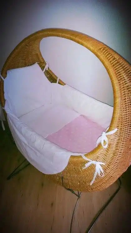 Gevlochten wiegmand met wit en roze beddengoed.