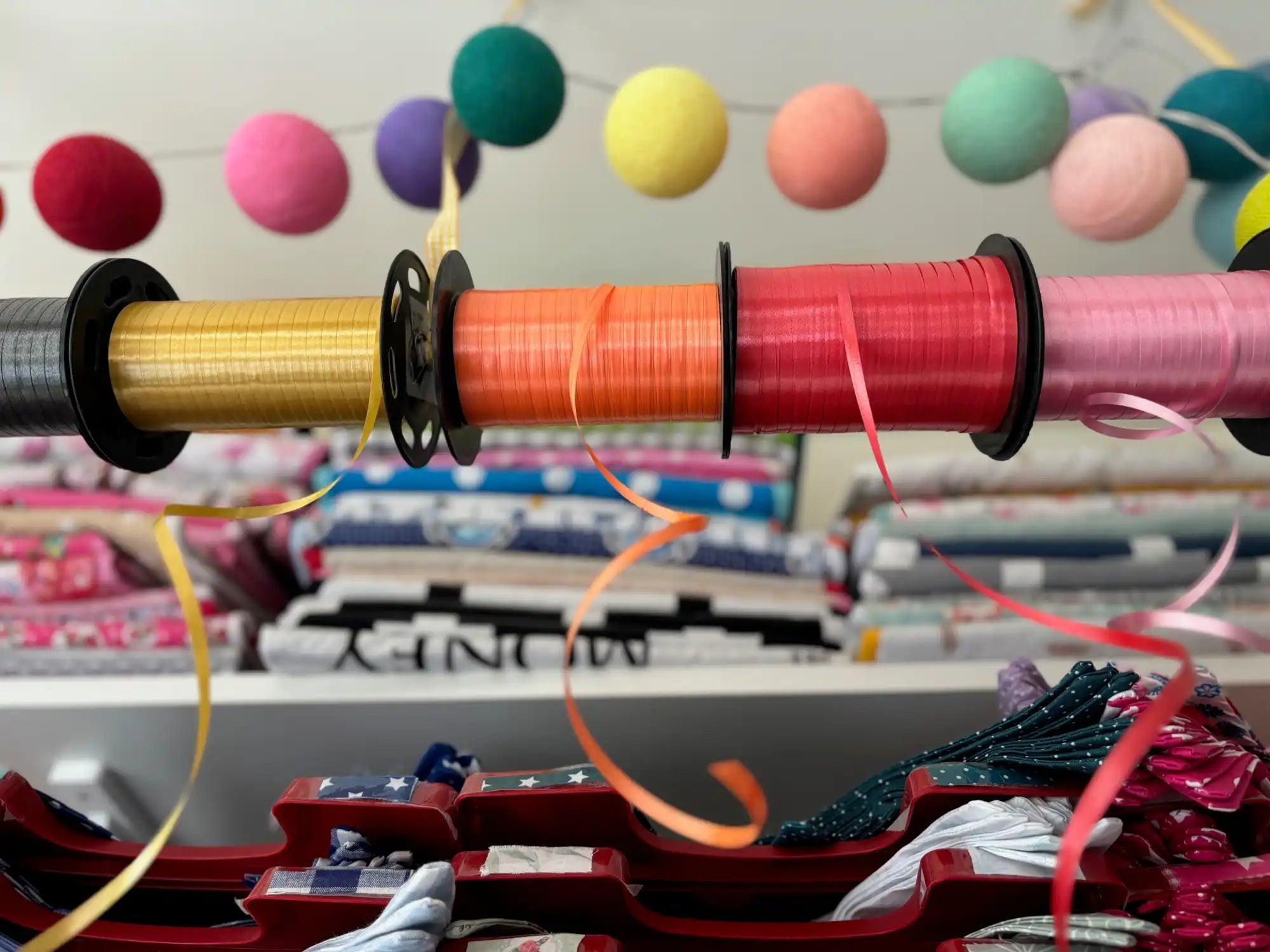 Een horizontale stok met vijf spoelen met kleurrijk lint, met enkele lintstrengen uitgelegd.