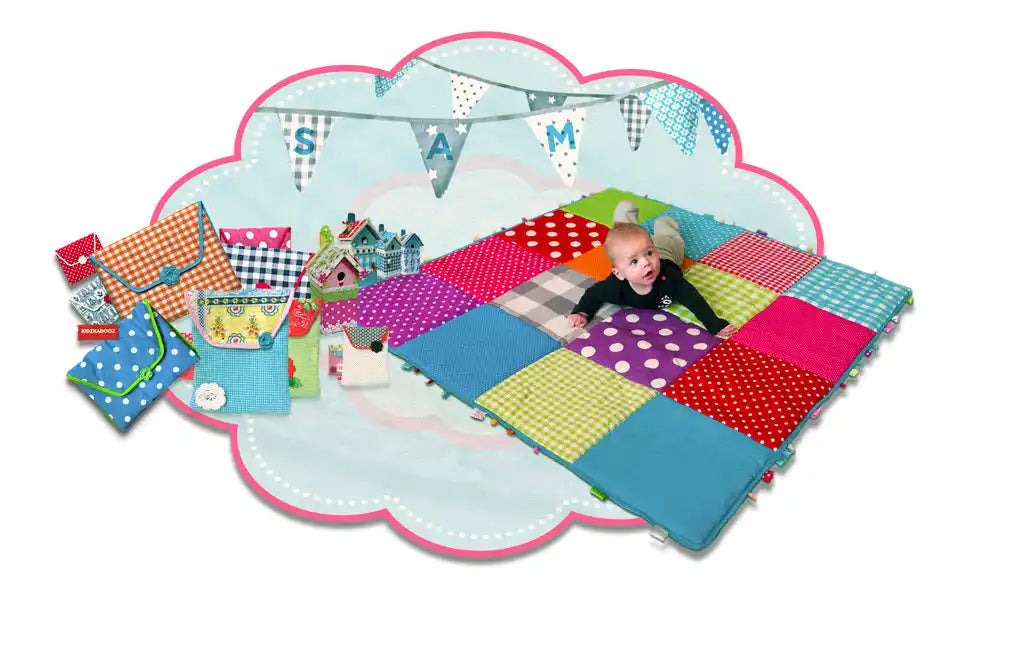 Een kleurrijk patchwork speelmat met een baby en verschillende gevilt accessoires met patronen.