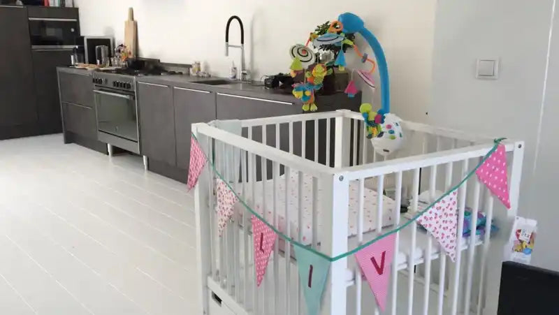 Witte houten babybedje met kleurrijke slingers.