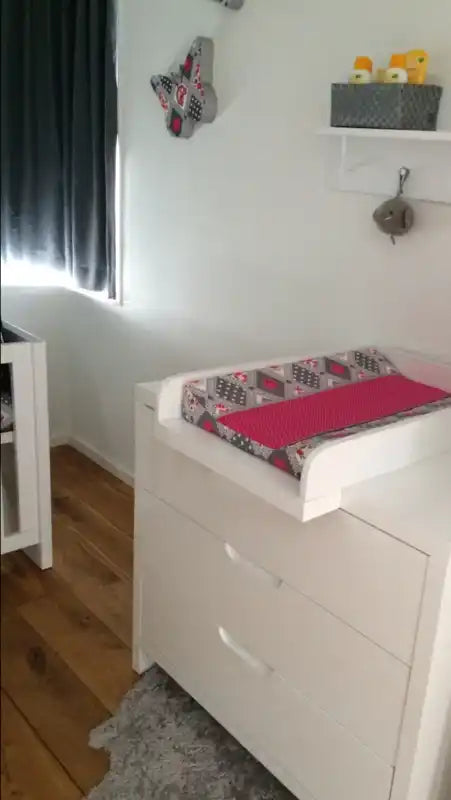 Wit houten verschoningskussen met twee lades en een verschoningskussen met een roze en grijs patroon.