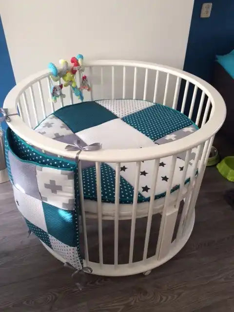 Een witte ovale wieg voor baby's met een patchwork matras en hangt organiser.