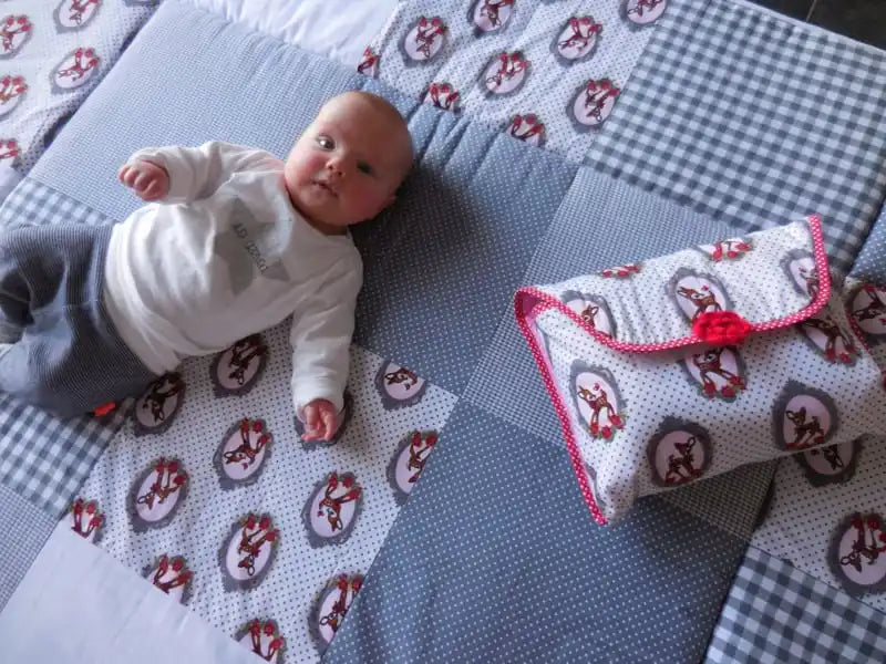 Een baby liggend op een gekleurd quilt naast een bijpassende zak.